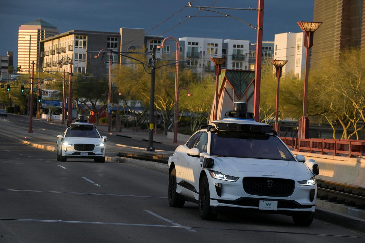 Two Waymo autonomous vehicles drive themselves down Central Avenue in Phoenix, Arizona